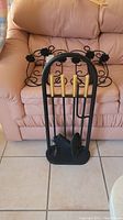 Photo of fireplace utensil set with black metal stand and gold-handled tools in front of couch, with black metal candle holders behind it.