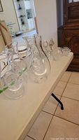 Four clear glass pitchers in varying shapes arranged on a white folding table.