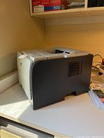 HP laser printer on desk, beige and black, showing left side and paper tray