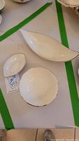 Three white Lenox candy dishes arranged on a table: an oval with a silver tone trim, a scalloped round with gold tone trim, and a long leaf-shaped with silver tone trim