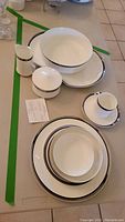 Photo showing stacked plates, bowls, cup and saucer, creamer, and sugar bowl, illustrating the set pieces and bone china style with silver trim.