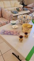 Lots of various ceramic items, including Toby mugs, decorative plates, cheese bowl with spreader, and signed bowl on table.
