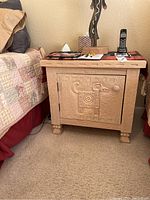 Front view of the wood nightstand next to bed, showing carved animal design on the cabinet door.