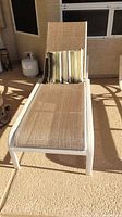 Full view of the outdoor chaise lounge chair showing white frame, beige fabric, and striped cushion.