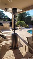 Full view of the standing outdoor propane heater placed on patio near pool and chairs.
