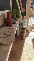 Two foam pool noodles, floating mat, various candle holders, basket with live plants, and a sandstone clock displayed on shelves and floor in outdoor area.