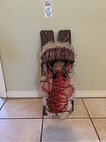 Front view showing the full cradleboard with the doll wrapped in colorful patterned fabric and fur trim.