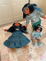Photo of three Southwest style dolls on a quilted bedspread showing their various clothing and sizes, including the tallest doll standing, the medium one lying down, and the smallest sitting