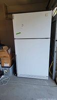 Front view of white Whirlpool refrigerator with two doors, top freezer and larger refrigerator below. Includes sticker on freezer door.