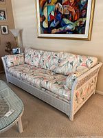 Front angle view of white wicker sofa with floral cushions, showing the full couch and pattern.