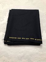 Folded black pure superfine new wool fabric with gold printed text on edge stating origin and material.