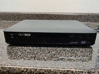 Front view of the Cisco 9865HD Nextbox PVR showing power button and brand logos.