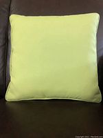 Front view of a lime green square cushion against a dark background, showing clean lines and smooth fabric surface.