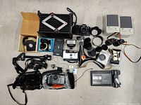 Overview of all items including cameras, binoculars, flashes, batteries, and camera accessories laid out on floor.