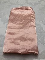 Neatly folded rose coloured sateen fabric placed on a patterned surface.