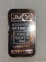 Close-up photo of a JM silver bar showing assay marks, purity, weight, and serial number.