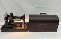 Singer black sewing machine with gold decals, hand crank, electric motor attached, alongside the bentwood dome case on a white backdrop.
