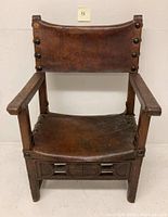 Front view of an 18th century Spanish armchair made from walnut wood and leather with large nail heads securing the leather backrest and seat.