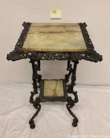 Full view of the antique plant stand showing the marble top, cast iron ornate frame, curved legs, and smaller marble shelf near the base.