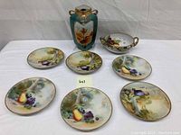 Photo showing six hand painted fruit and nature scene porcelain plates, one bowl, and one tall vase.