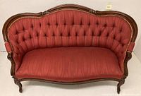 Front view of antique Victorian tufted settee upholstered in deep red fabric with wooden frame and button tufting.