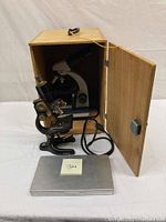 Optical microscope inside wooden carrying case, metal specimen tin in foreground