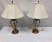 Pair of Mid-Century Modern brass and crystal lamps with beige fabric shades on white table against grey backdrop.
