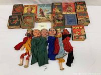 Overview of 12 vintage children's storybooks with colorful covers featuring characters like Tarzan, Jackie Cooper, Little Orphan Annie, The Lone Ranger, Popeye, Shirley Temple, and more, displayed with 6 hand puppets.