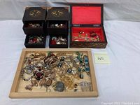 Four vintage wooden jewelry boxes shown, three smaller square boxes with inlaid lids and one larger rectangular box with red interior lining, filled with costume jewelry pieces.