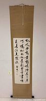 Full view of hanging scroll displaying black ink calligraphy on paper mounted on tan backing