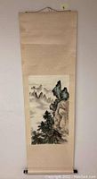 Full vertical view of the beige hanging scroll with the painted mountain landscape centered on paper and mounted on silk fabric.