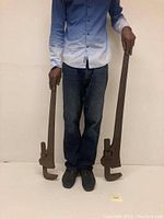 Full view showing two large vintage rigid pipe wrenches next to a person for size comparison, measuring 32 and 41.5 inches in length respectively.