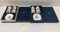 Two open navy blue Royal Worcester boxes each containing four demitasse cups and saucers.