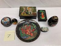 Full view of the lot showing various lacquered decorative items including eggs, boxes, and a plate with folk art hand-painted scenes.