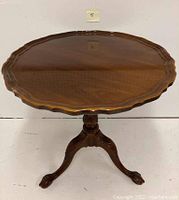 Full view of the glossy wooden piecrust scalloped round top side table with clawfoot legs.