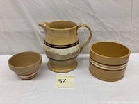 Photo showing three pieces of vintage yellow ware pottery: a pitcher, a small textured bowl, and a butter crock with brown and white band stripes.