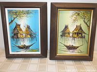 Pair of framed tiki hut houseboat paintings, one blue tone and one green tone.