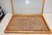 Top view of opened display case showing brown velvet-like fabric cushion liner inside the wood frame with hinged glass top.
