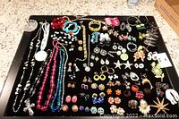 Overview photo of all jewelry pieces laid out on a black surface showing necklaces, earrings, pins, bracelets, and rings.