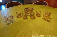 Wide view of entire barware set including ice bucket, 4 short glasses, 4 stemmed cordial glasses and 4 other stemmed cordial glasses arranged on a green cloth.