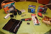 Overview photo showing all tools laid out on a green table, including boxed Black & Decker drill, blue orbital sander, red sanding tool, electric screwdriver with case and soldering iron kit.