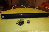Full view of the iLive sound bar, power cord, and remote control arranged on a green cloth-covered table.
