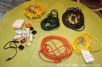 Lot contents showing five heavy duty outdoor extension cords in various colors along with multiple plug adapters and timers on a green surface.