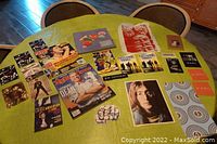 Top-down photo showing a collection of vintage rock collectibles on a table, including postcards, magazines, buttons, patches, and books.