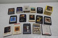 Photo showing multiple 8 track tapes arranged on a white patterned cloth, displaying various artists and titles including Dean Martin and Johnny Cash.