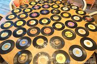 Wide view of the collection of 7-inch 45 RPM vinyl records arranged on a table with visible colorful paper labels, showing the overall quantity and condition range