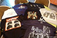Photo showing ten assorted rock and tourist themed t-shirts laid out on chairs and floor. Includes Beatles Hard Day's Night, Queen cropped long sleeve, London, and Brighton shirts.