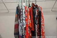 Photo showing 12 ladies blouses and tops hanging in a closet, various colors and patterns including plaid, floral, and abstract prints.