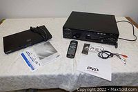 The lot displayed showing two black disc players on a table: Samsung Blu-Ray 3D player on left, Apex 3-disc carousel DVD player on right with remote, cables, and manuals.