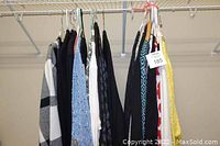 Photo showing 21 ladies sweaters and tops hanging on a clothing rack in a closet, various colors and patterns visible.
